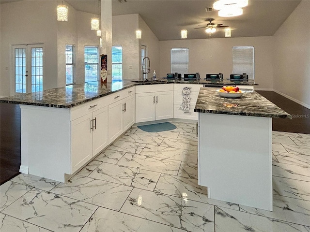 kitchen with sink, hanging light fixtures, a kitchen island, dark stone countertops, and white cabinets