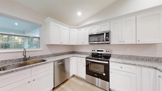 kitchen featuring vaulted ceiling, sink, white cabinets, stainless steel appliances, and light stone countertops