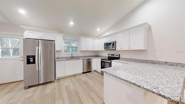 kitchen featuring sink, kitchen peninsula, stainless steel appliances, light stone countertops, and white cabinets