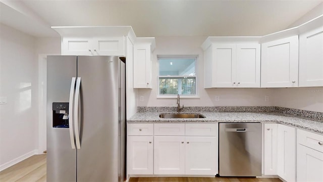 kitchen featuring sink, appliances with stainless steel finishes, white cabinetry, light stone counters, and light hardwood / wood-style floors