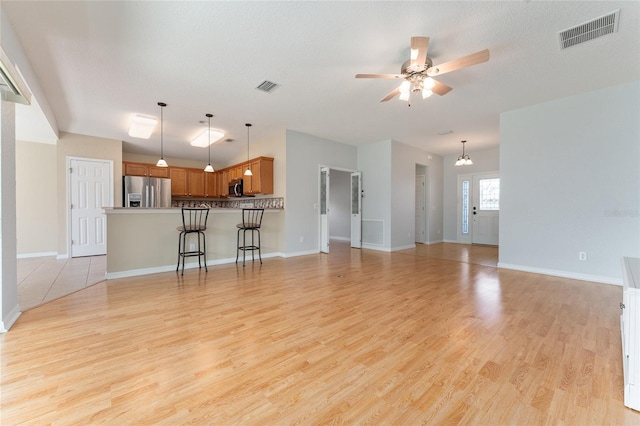 unfurnished living room featuring light hardwood / wood-style floors, a textured ceiling, and ceiling fan with notable chandelier