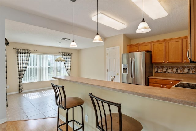 kitchen featuring kitchen peninsula, stainless steel fridge, a breakfast bar, light hardwood / wood-style flooring, and pendant lighting