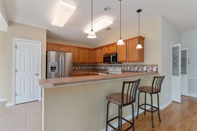 kitchen with stainless steel appliances, a textured ceiling, kitchen peninsula, and a kitchen breakfast bar