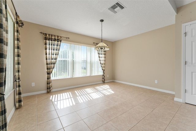 spare room featuring a chandelier, light tile patterned flooring, and a textured ceiling