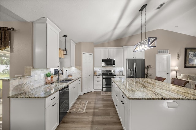 kitchen featuring white cabinets, appliances with stainless steel finishes, decorative light fixtures, and vaulted ceiling