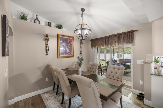 dining space with light wood-type flooring, an inviting chandelier, and vaulted ceiling