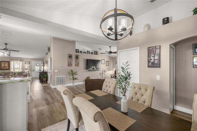 dining area with wood-type flooring, ceiling fan with notable chandelier, and vaulted ceiling