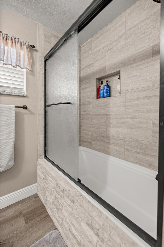 bathroom featuring bath / shower combo with glass door, wood-type flooring, and a textured ceiling