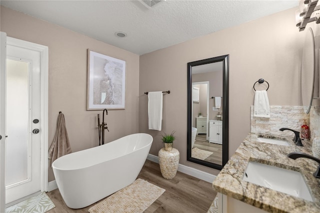 10291 SE 42nd Ter, Belleview, FL 34420 - bathroom with wood finished floors, a freestanding tub, double vanity, baseboards, and a textured ceiling