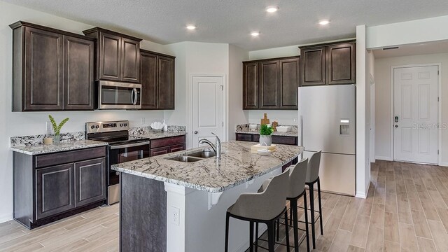 kitchen featuring a breakfast bar area, wood finish floors, a sink, appliances with stainless steel finishes, and an island with sink