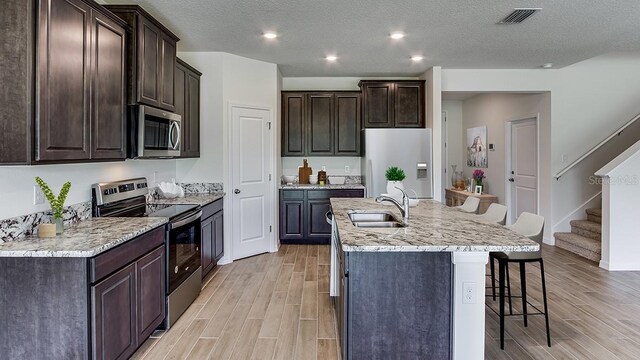 kitchen with appliances with stainless steel finishes, wood tiled floor, a kitchen island with sink, and a kitchen bar