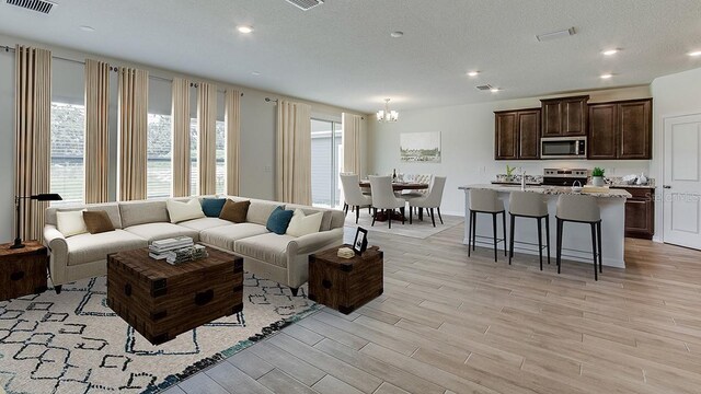 living area featuring a notable chandelier, light wood finished floors, recessed lighting, visible vents, and a textured ceiling