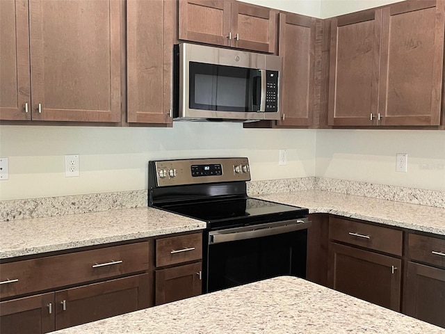 kitchen featuring light stone counters, dark brown cabinetry, and stainless steel appliances