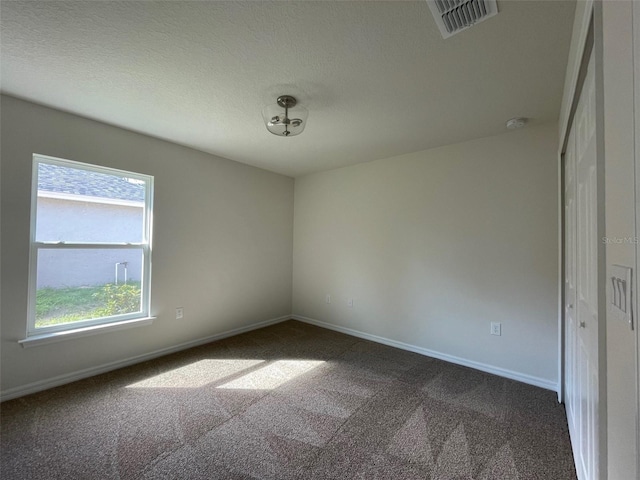 spare room with dark colored carpet, a textured ceiling, and a wealth of natural light