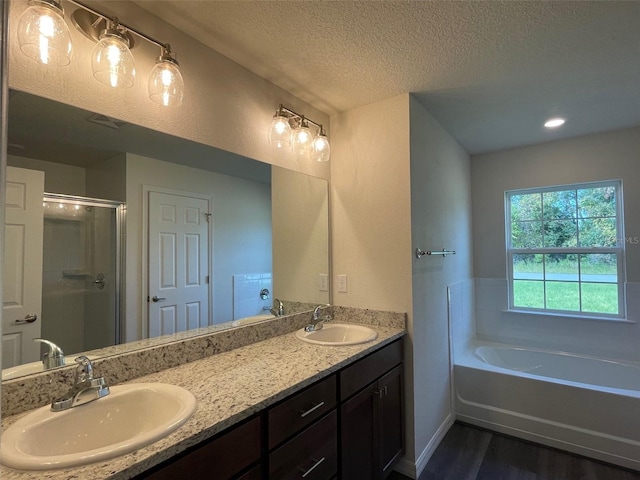 bathroom with plus walk in shower, vanity, wood-type flooring, and a textured ceiling