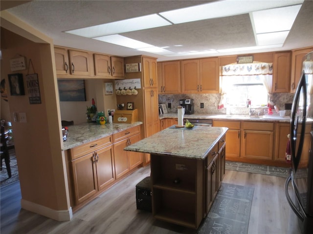 kitchen featuring light hardwood / wood-style floors, black fridge, light stone countertops, and a kitchen island