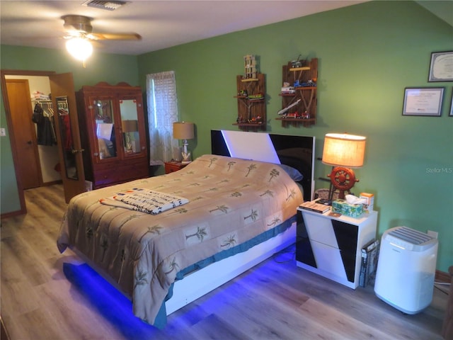 bedroom with a closet, ceiling fan, wood-type flooring, and a walk in closet