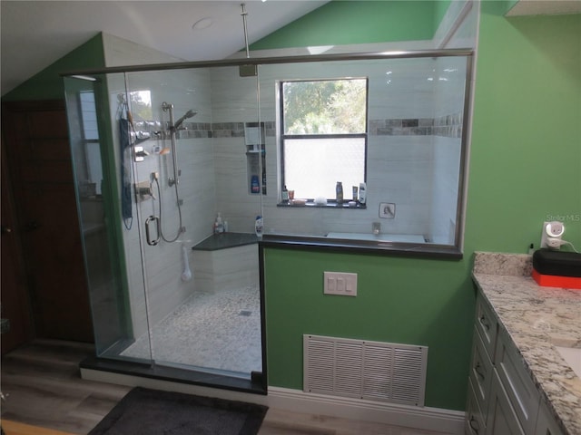 bathroom featuring vanity, hardwood / wood-style flooring, walk in shower, and vaulted ceiling