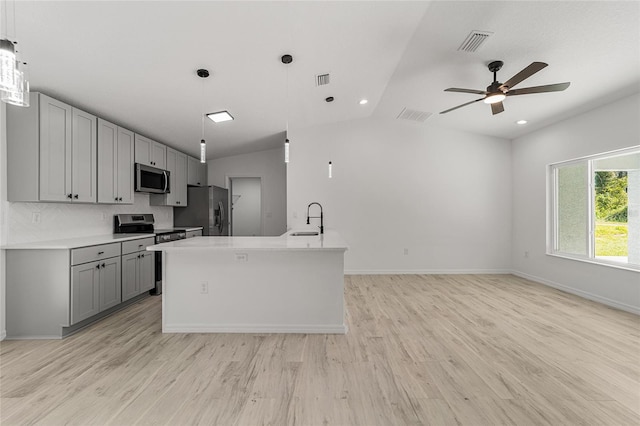 kitchen featuring lofted ceiling, an island with sink, sink, gray cabinetry, and stainless steel appliances