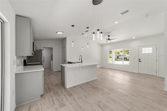 kitchen with an island with sink, hanging light fixtures, light hardwood / wood-style flooring, vaulted ceiling, and range