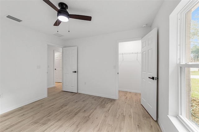 unfurnished bedroom featuring a closet, a walk in closet, light hardwood / wood-style floors, and ceiling fan