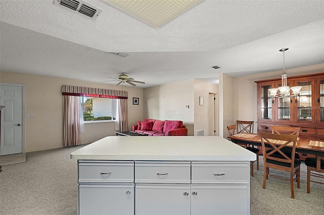 kitchen with a textured ceiling, light colored carpet, and pendant lighting