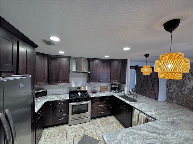 kitchen featuring wall chimney range hood, sink, appliances with stainless steel finishes, hanging light fixtures, and a barn door