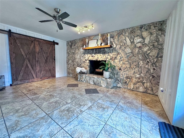 unfurnished living room with a stone fireplace, a barn door, and ceiling fan