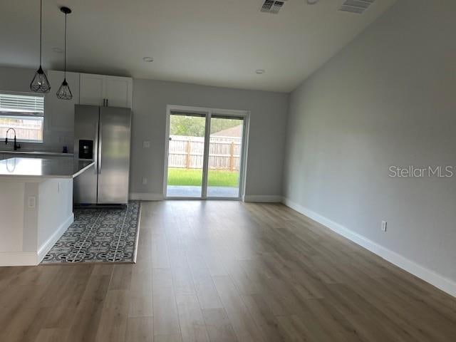 kitchen with light hardwood / wood-style flooring, stainless steel refrigerator with ice dispenser, sink, decorative light fixtures, and white cabinetry