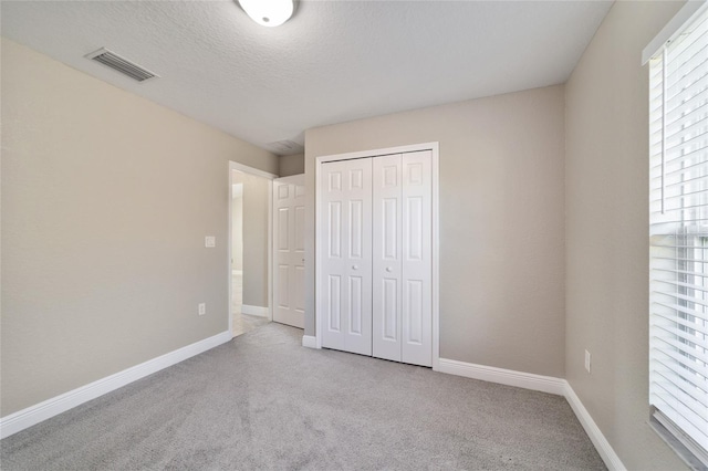 unfurnished bedroom with a closet, a textured ceiling, and light colored carpet