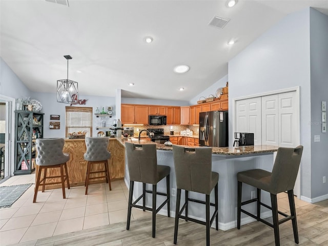 kitchen with black appliances, lofted ceiling, a kitchen bar, and light wood-type flooring