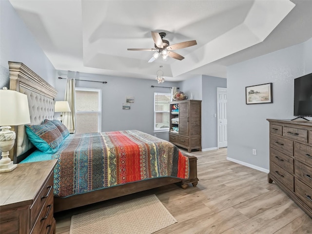 bedroom featuring a raised ceiling, multiple windows, ceiling fan, and light wood-type flooring