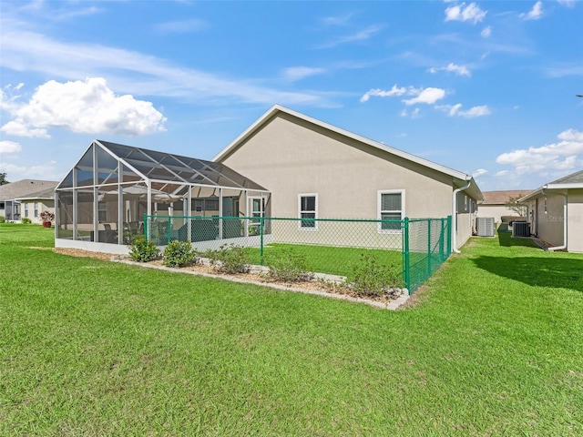 rear view of property with central air condition unit, glass enclosure, and a lawn