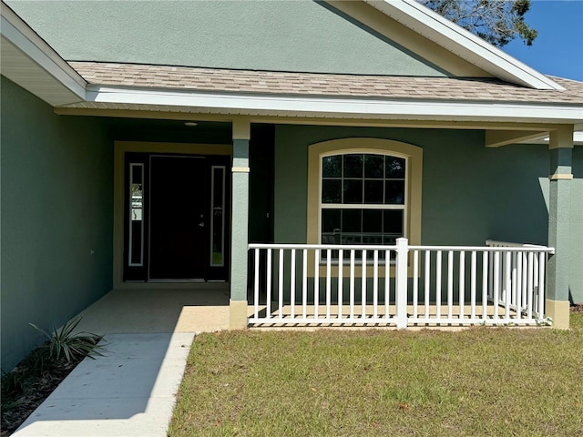 view of exterior entry with a porch, a shingled roof, and stucco siding