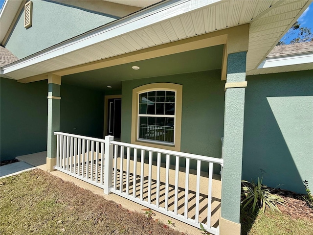 entrance to property featuring a shingled roof, covered porch, and stucco siding