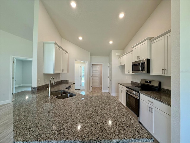 kitchen with a peninsula, a sink, white cabinets, appliances with stainless steel finishes, and dark stone countertops