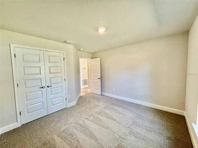 unfurnished bedroom featuring a closet, light colored carpet, visible vents, and a textured ceiling