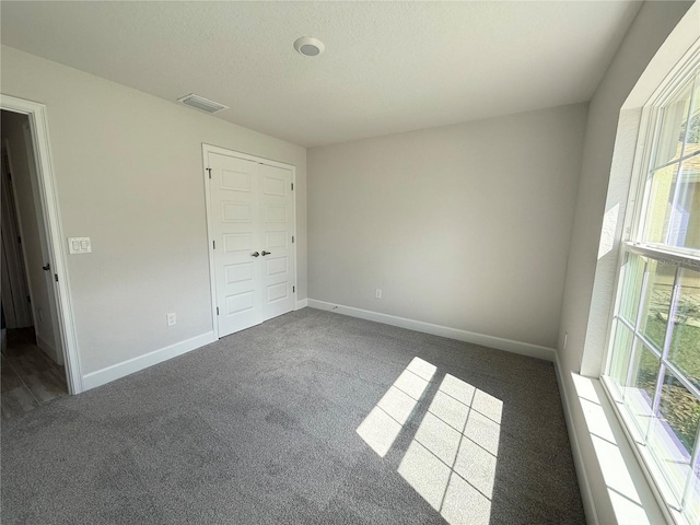 spare room with a textured ceiling, dark carpet, visible vents, and baseboards