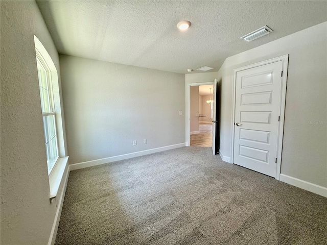 unfurnished bedroom with baseboards, visible vents, a textured wall, a textured ceiling, and carpet floors