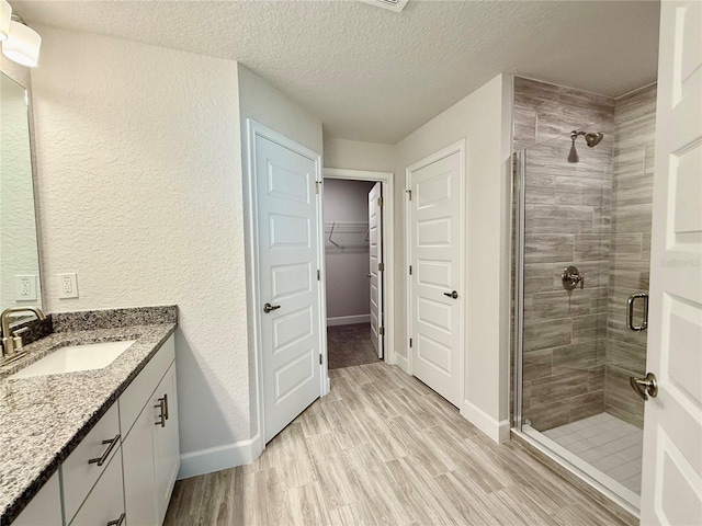 full bath featuring a walk in closet, a shower stall, vanity, and wood finished floors