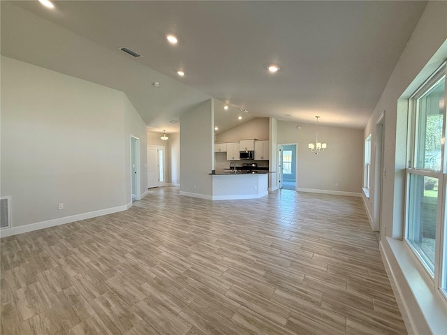 unfurnished living room with light wood-type flooring, a chandelier, a wealth of natural light, and lofted ceiling