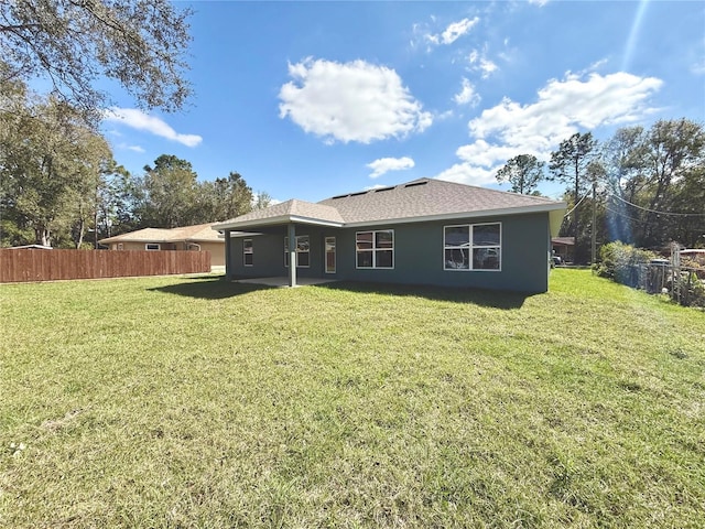 rear view of property with stucco siding, fence, and a lawn