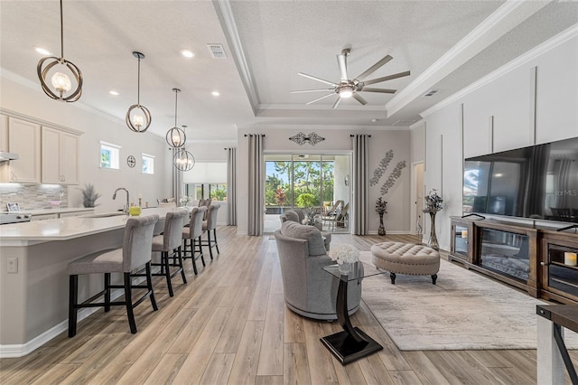 living room featuring light hardwood / wood-style flooring, a textured ceiling, crown molding, and a tray ceiling