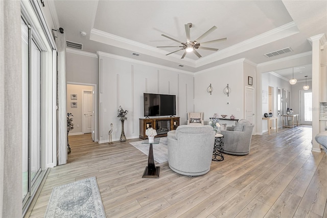 living room featuring light hardwood / wood-style flooring, ceiling fan, ornamental molding, and a raised ceiling