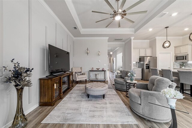 living room with ornamental molding, light wood-type flooring, ceiling fan, and a tray ceiling