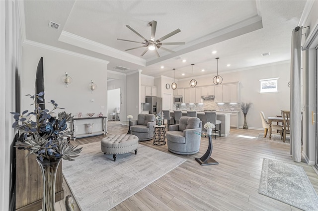 living room featuring ornamental molding, light wood-type flooring, and a tray ceiling