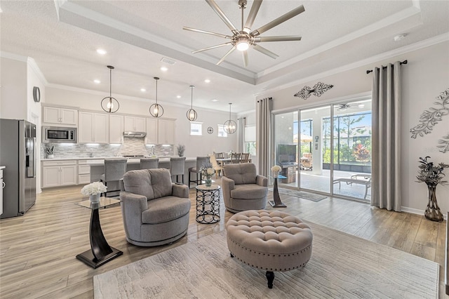 living room with ornamental molding, light wood-type flooring, a textured ceiling, a tray ceiling, and ceiling fan