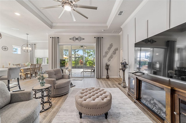 living room with a tray ceiling, a healthy amount of sunlight, light hardwood / wood-style floors, and crown molding