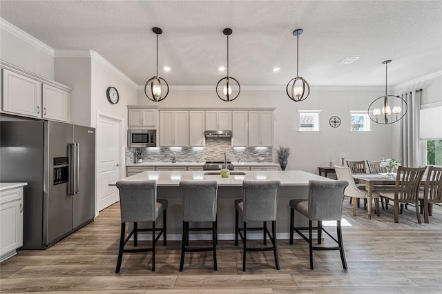 kitchen with pendant lighting, stainless steel appliances, wood-type flooring, and a kitchen island with sink