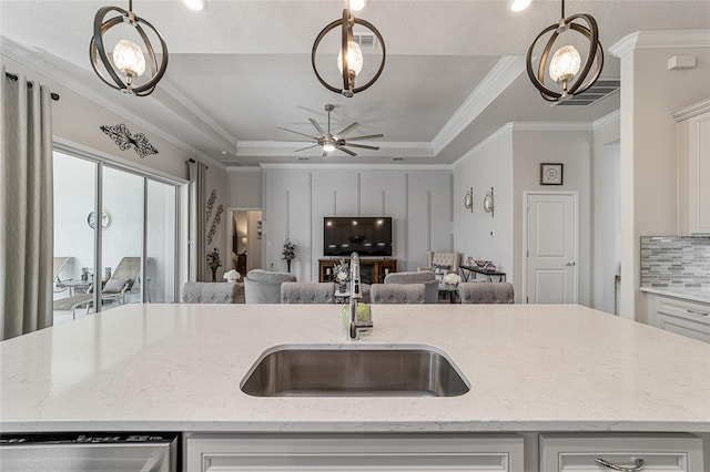 kitchen with a center island with sink, sink, white cabinetry, light stone countertops, and hanging light fixtures